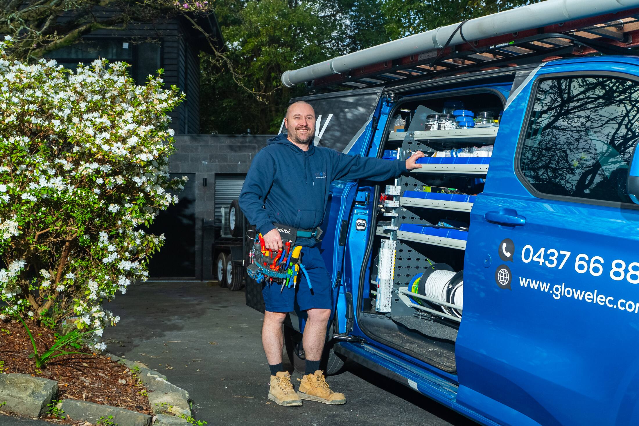 Michael at the open van, tool belt on, before a switchboard upgrade